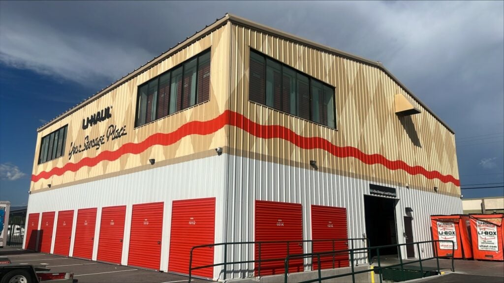 Exterior of a U-Haul storage facility with red storage unit doors and large windows, featuring a beige and red-striped façade.